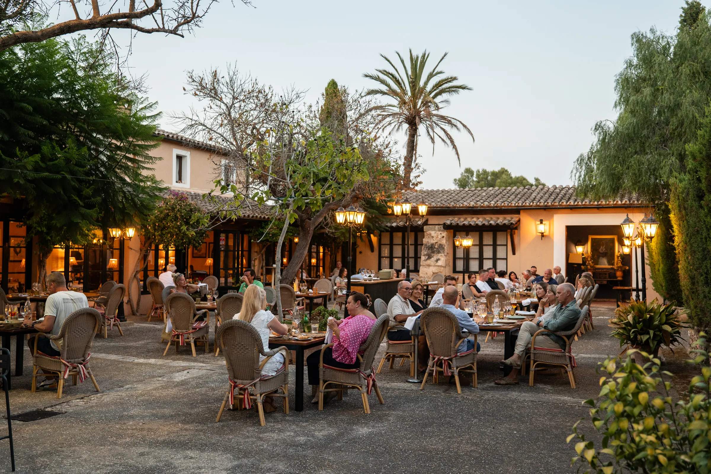 Patio de Ca’s Pastor al atardecer, con comensales y las lámparas encendidas